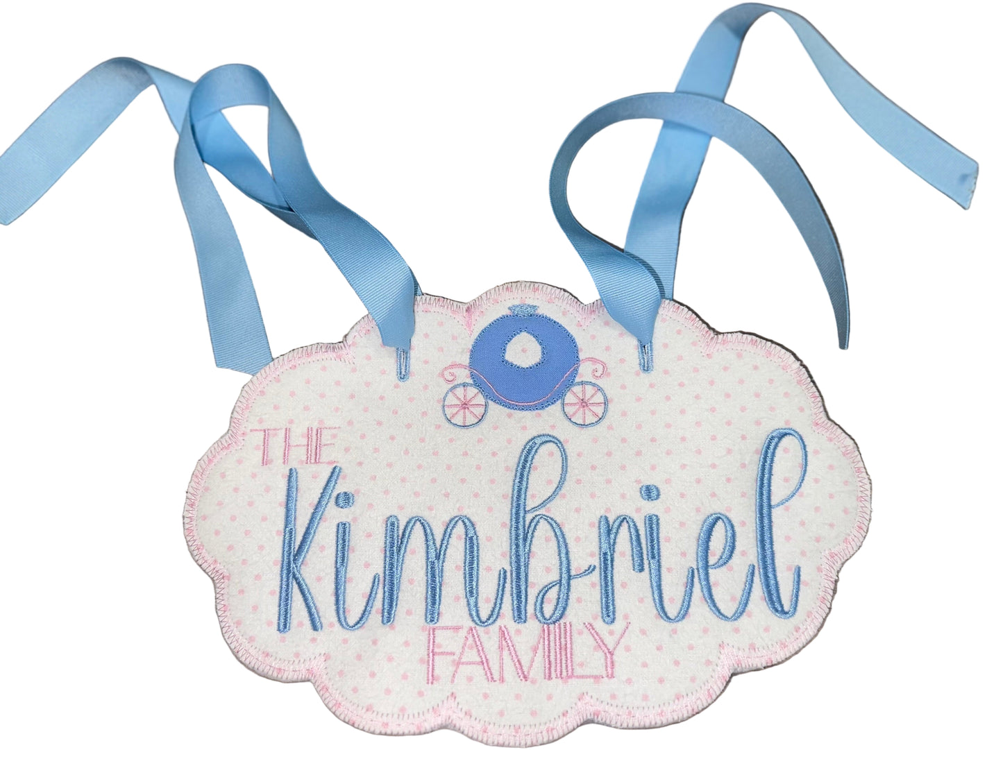 Decorative sign with 'The Kimbriel Family' text and blue ribbons on a wooden surface