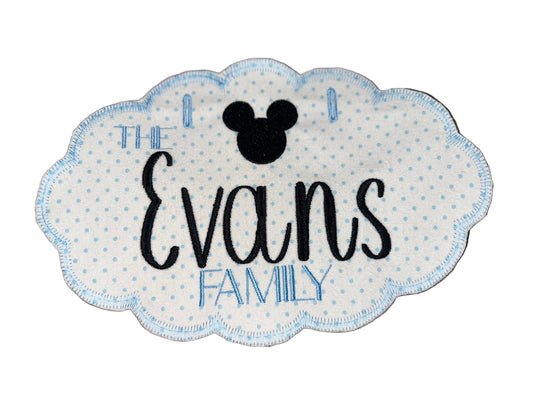 Embroidered patch with 'The Evans Family' text and Mickey Mouse head on a wooden surface