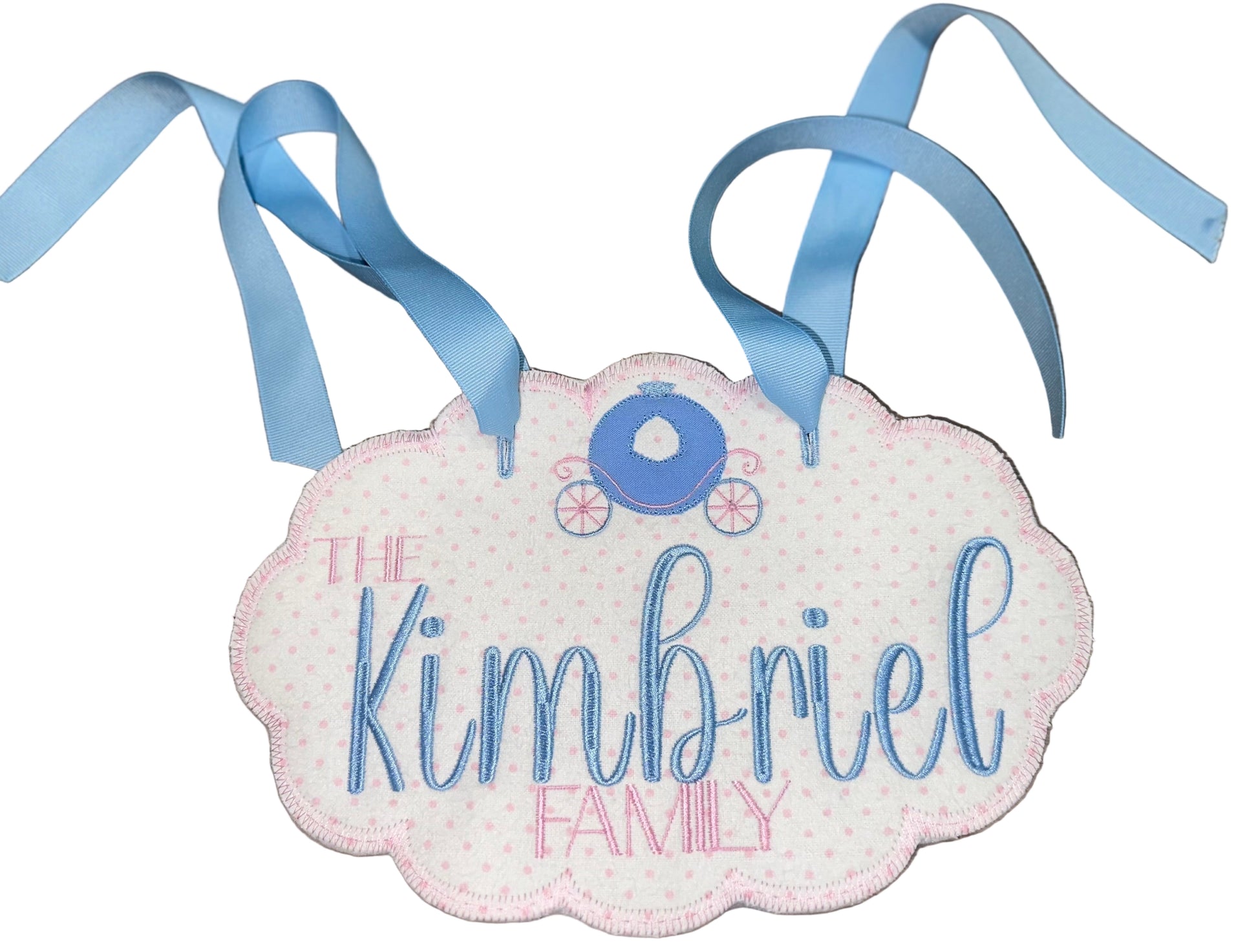 Decorative sign with 'The Kimbriel Family' text and blue ribbons on a wooden surface